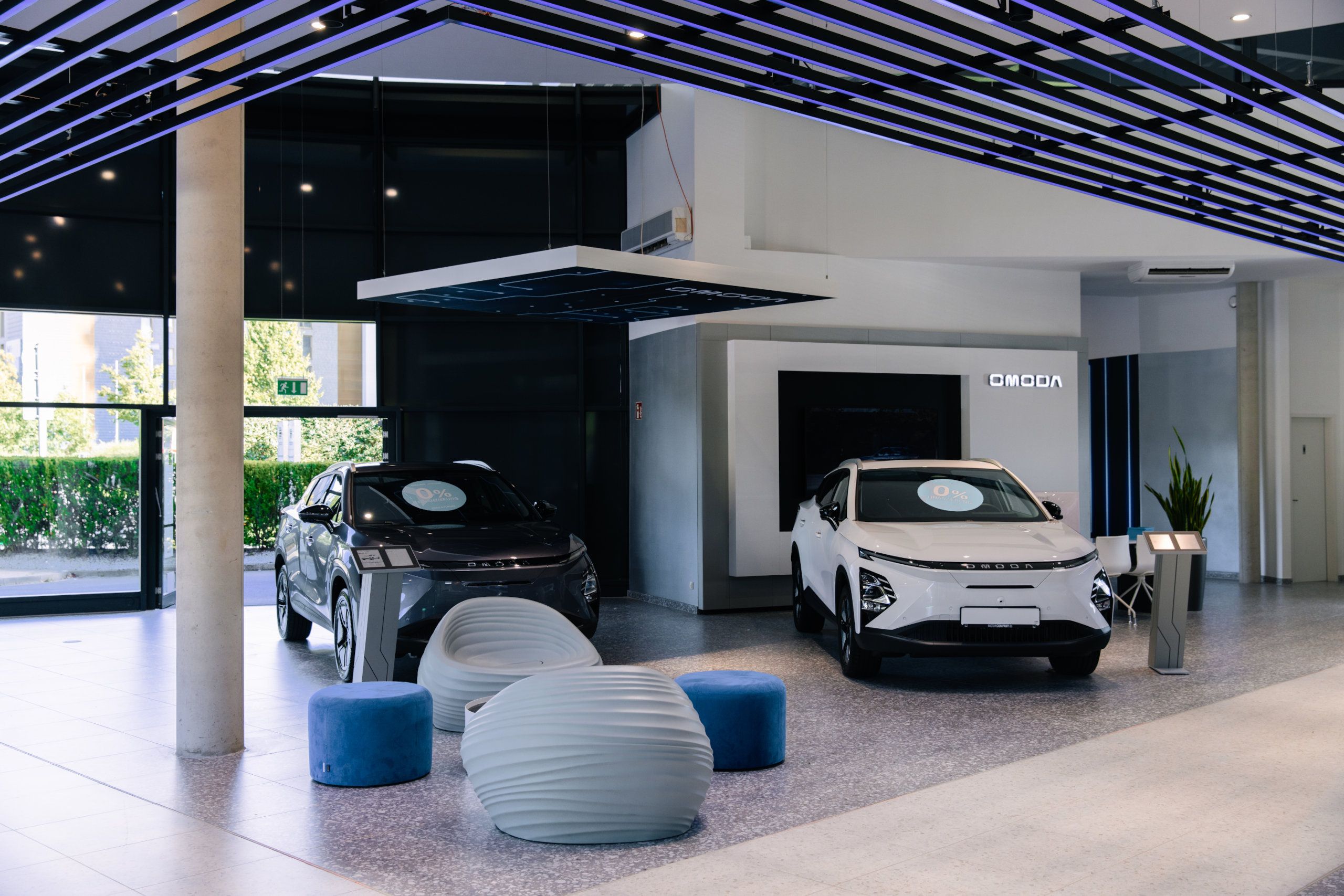 Zwei OMODA-SUV in Grau und Weiß im Showroom eines Handelspartners, dahinter die OMODA-Markenwand
