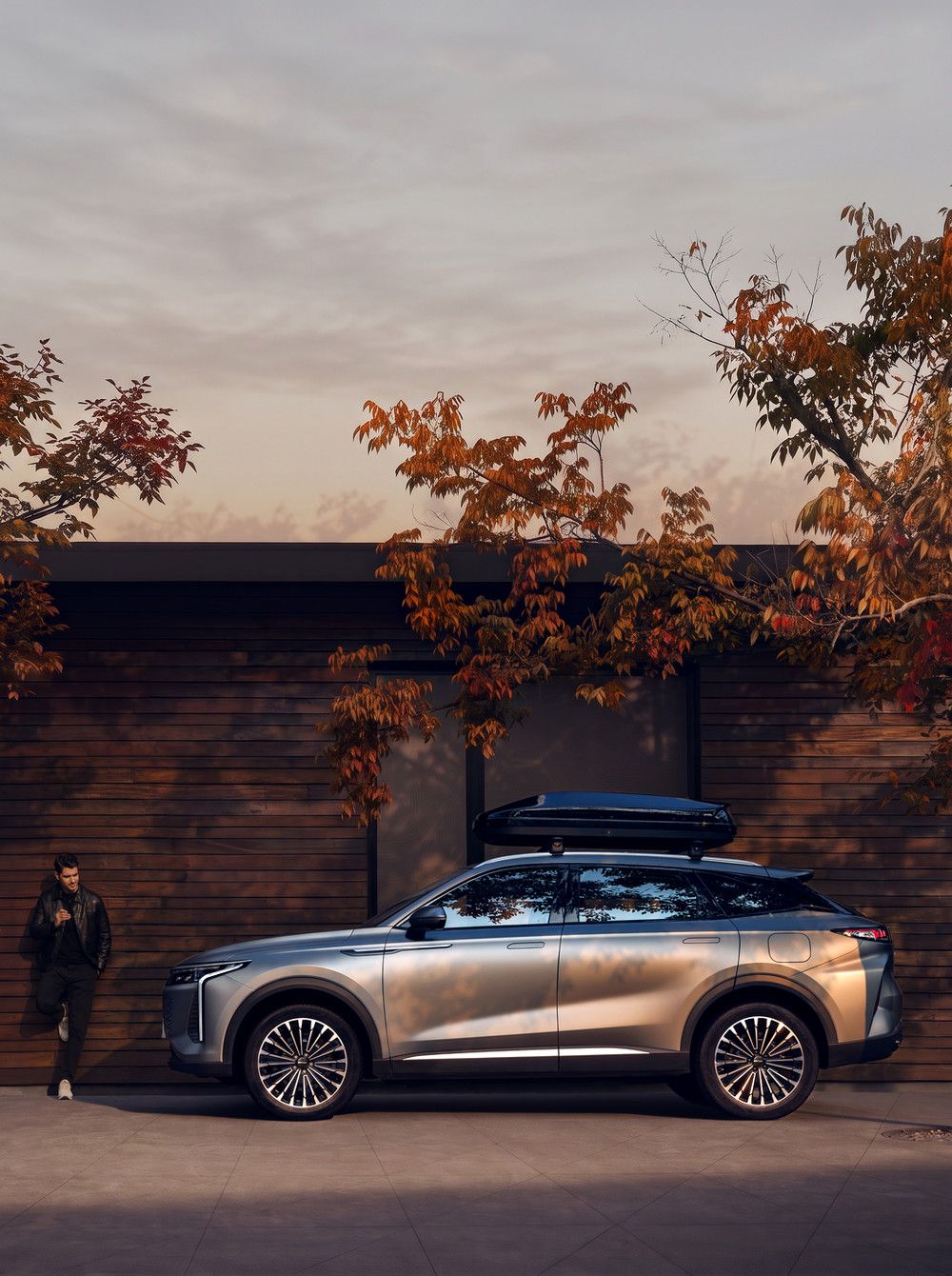 OMODA 9 PHEV mit Dachbox und Fahrer vor Holzfassade