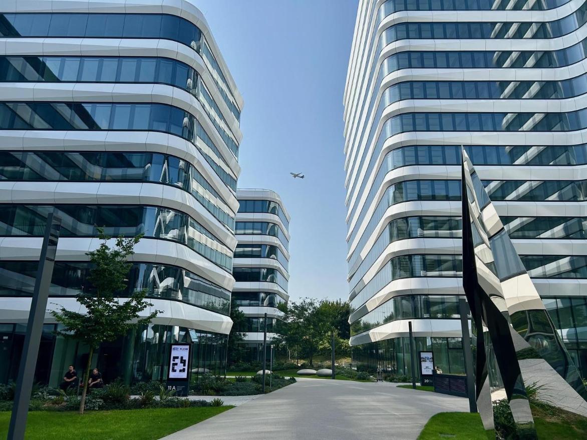 Bürogebäude mit geschwungenen Glasfassaden in Gateway Gardens, darüber ein startendes Flugzeug